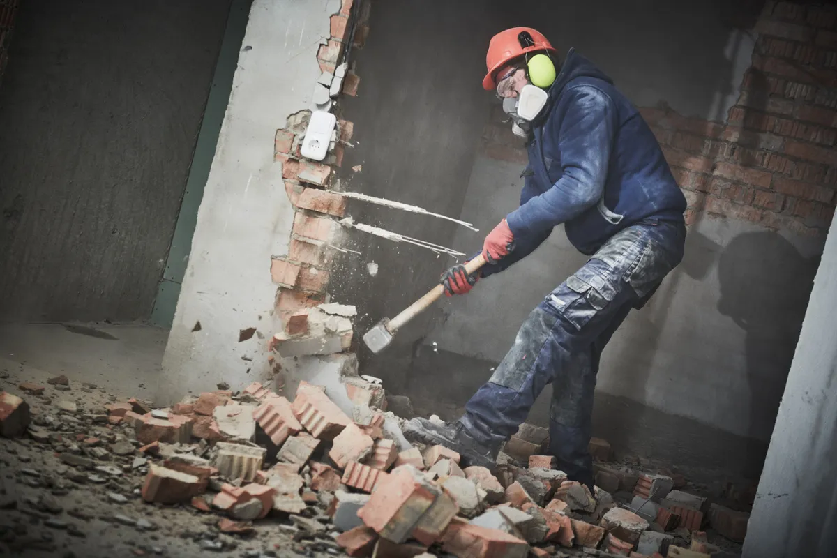 Belys Bau GmbH – Bauunternehmen – Abbruch- und Umbauarbeiten. Arbeiter mit Vorschlaghammer zerstört Wand